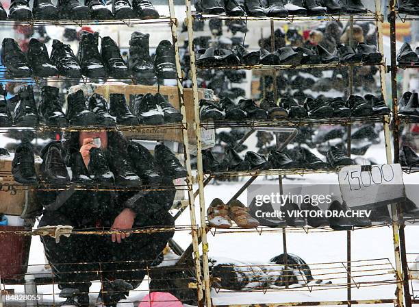 Vendor drinks tea under snowfall at an open-air second-hand clothing and goods market outside Minsk in Zhdanovichi on February 17, 2009. The average...