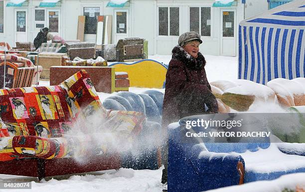 Woman brushes snow off a sofa at an open-air second-hand clothing and goods market outside Minsk in Zhdanovichi on February 17, 2009. The average...