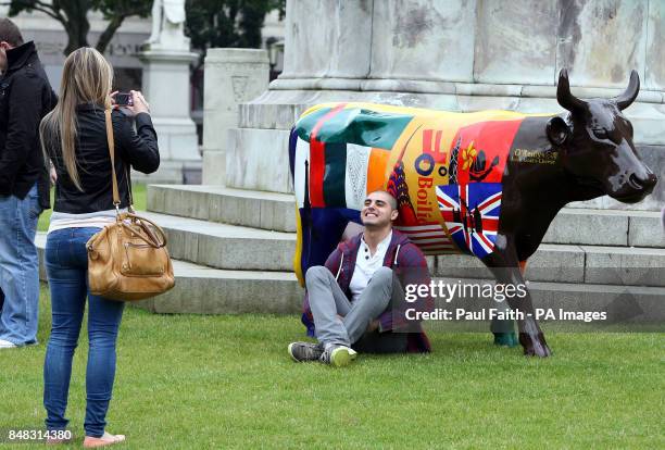 Man has his picture taken with one of the decorated cows that form part of the CowParade exhibition in the grounds of City Hall, Belfast.