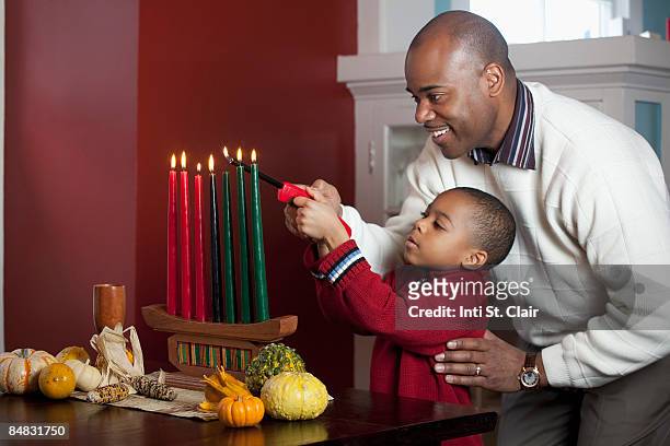 dad and son lighting kinara for kwanzaa - kwanzaa stock pictures, royalty-free photos & images