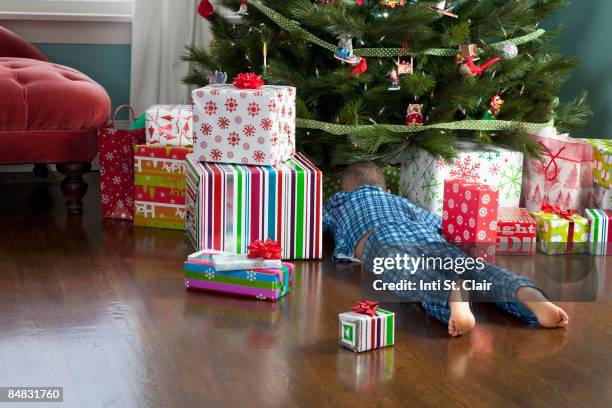 curious boy digging through presents under tree - christmas presents under tree stock pictures, royalty-free photos & images