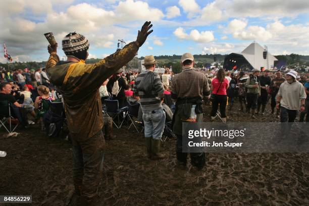 Photo of GLASTONBURY, a muddy festival goer holding watching a band on the Pyramid Stage at Glastonbury Festival, holding his arms in the air,...