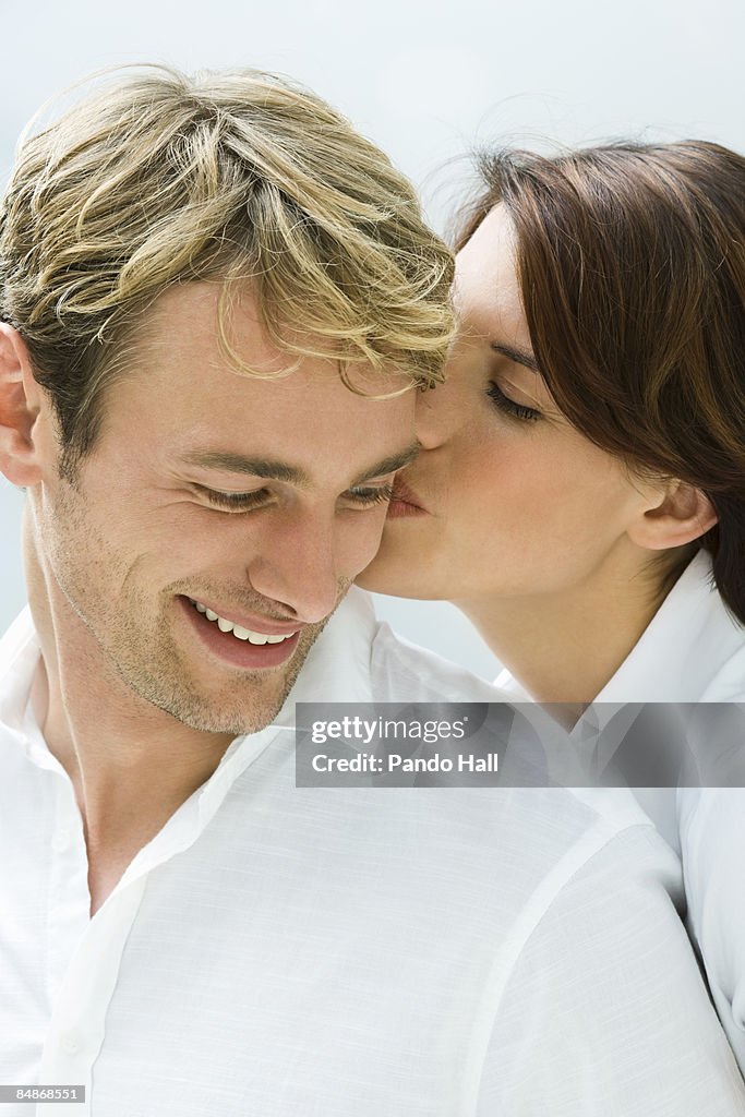 Woman kissing smiling man on cheek, close-up