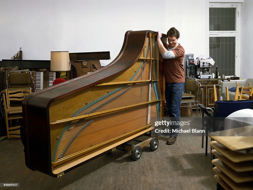 Man pushing piano on wheels in workshop