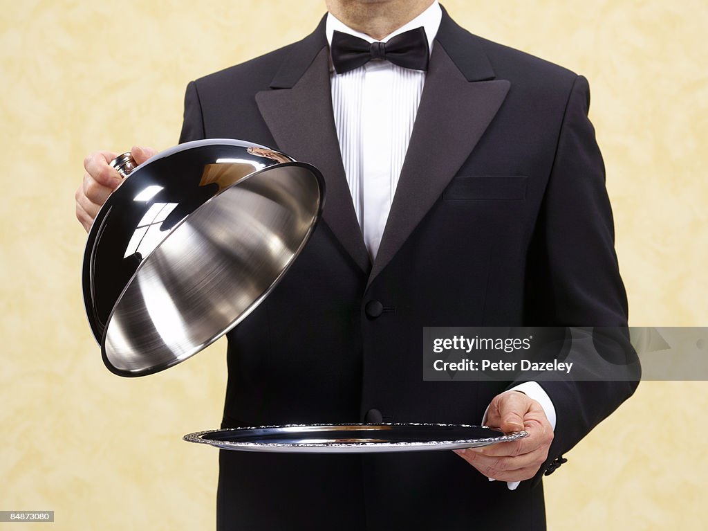 Butler waiter holding open domed silver tray.