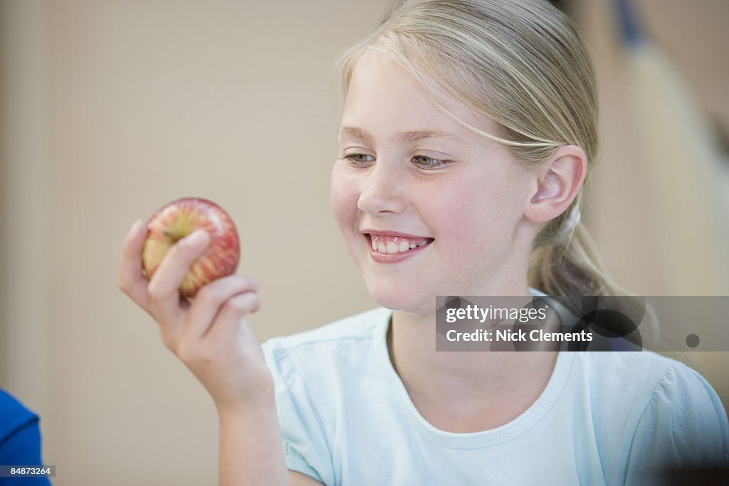 Girl (8-9) holding apple, smiling