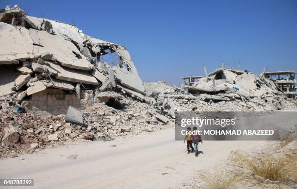 Syrian schoolchildren walk past destroyed buildings in a rebel-held area of the southern city of Daraa on September 17, 2017.