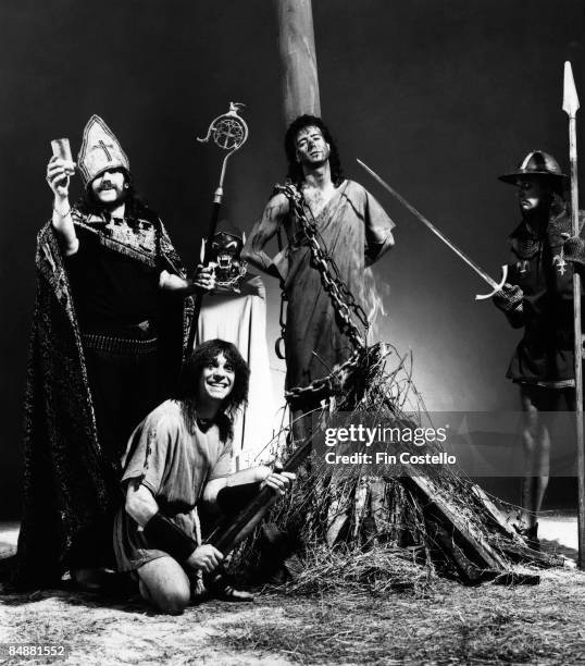 Photo of LEMMY and MOTORHEAD posed at a mock burning at the stake scene. Left to Right: Lemmy Mick "Wurzel" Burston, Phil Campbell, Pete Gill.