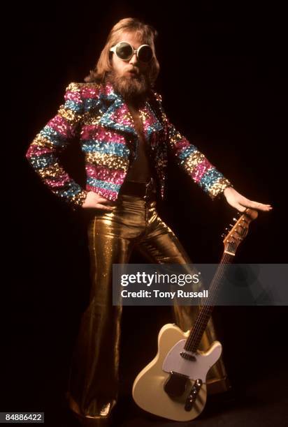 Generic 1970s glam rock musician wearing gold trousers, sparkling jacket, shades and a beard and holding a Telecaster guitar. Circa 1972.