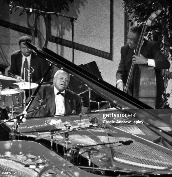 Circa 1970 Photo of Oscar PETERSON; Performing live onstage, behind grand piano, lid open, bass player and drummer in shot