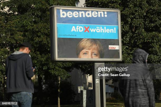 People walk past rotating billboards that show an election campaign poster of German Chancellor and Christian Democrat Angela Merkel intersecting...