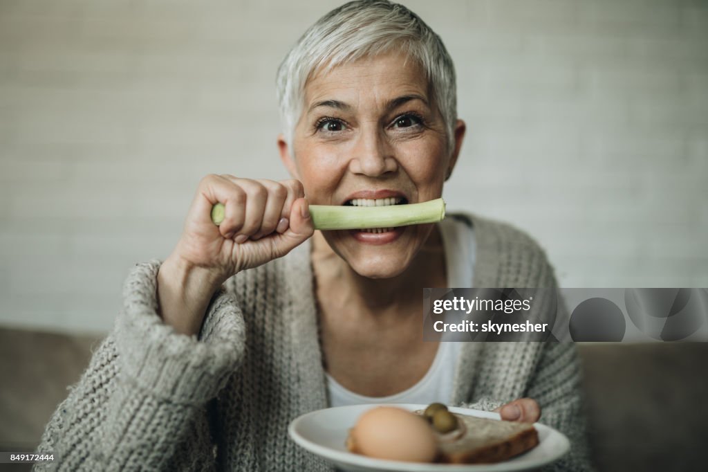 Mature woman biting celery and looking at camera.