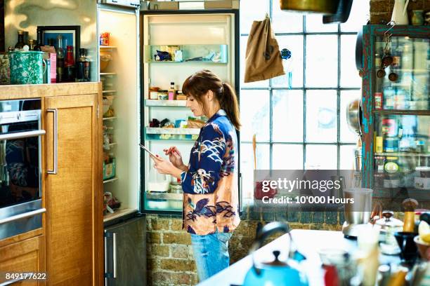 woman using tablet in kitchen - open fridge inside view stock pictures, royalty-free photos & images