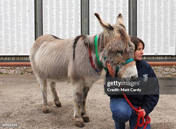 Amanda Gordon, groom, with Jubilee the donkey, stand in front of boards listing some of the names of people who have bequeathed money in their wills...