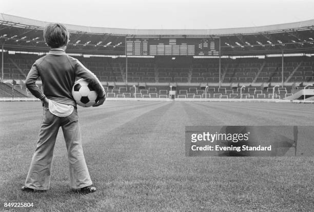 Child, Brendan Davey, looks at Wembley Stadium holding a soccer ball in his arm, London, UK, 2nd September 1977.
