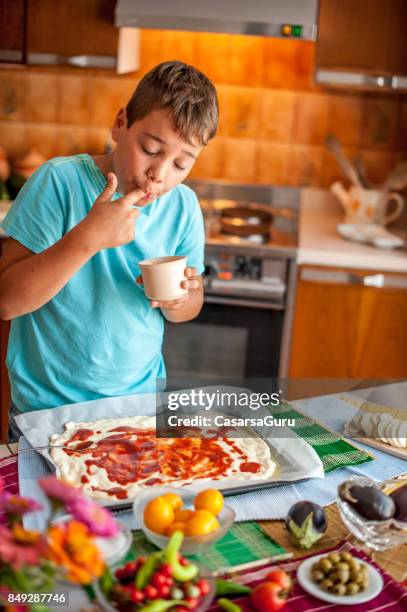 boy applying tomato sauce on pizza dough - baking dish stock pictures, royalty-free photos & images