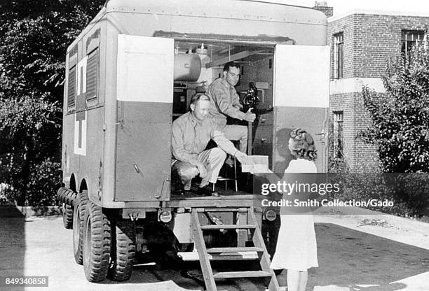 Two American Red Cross employees handing out medical supplies to a woman from a mobile unit, 1958. Image courtesy CDC.