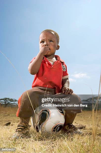 boy sitting on a soccer ball in the township. winterton, kwazulu-natal province, south africa - freek van den bergh stock pictures, royalty-free photos & images