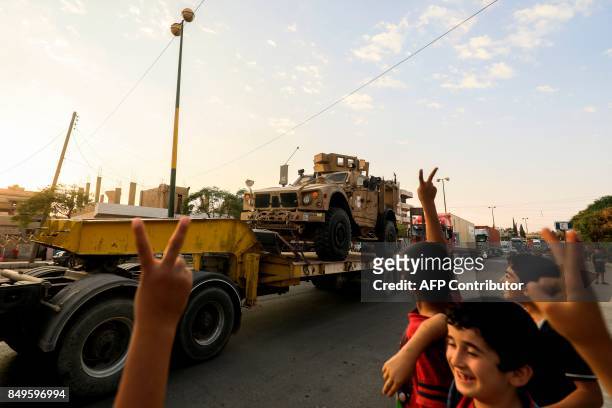 Children flash the victory gesture as a military convoy carrying US-made Oshkosh armoured vehicles, bulldozers, and arms headed for Syrian Democratic...