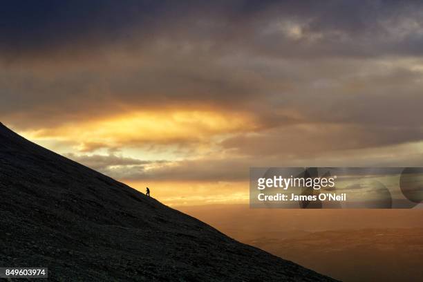 hiker walking uphill on ridge-line with dramatic sunset behind - uphill stock-fotos und bilder