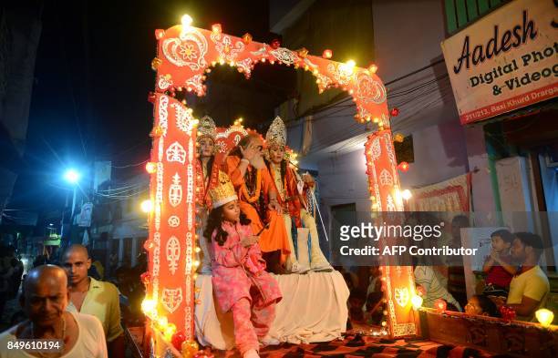 Hindu devotees watch a religious procession as young Indian artists sit on chariot while on the way to perfrom a traditional Ramleela drama, which...