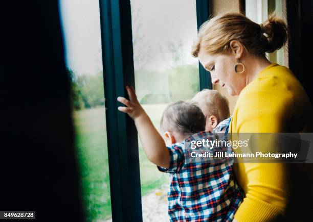 12 month old fraternal twins are assisted with standing on a window sill - twins boys stock pictures, royalty-free photos & images