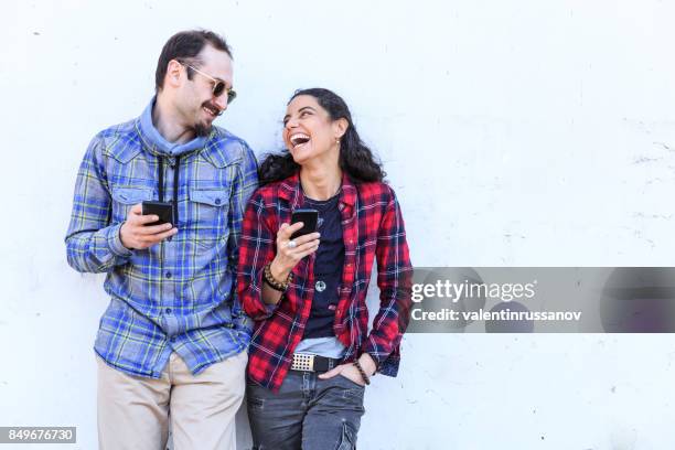 young couple laughing and using smart phones on stree - bending over backwards stock pictures, royalty-free photos & images