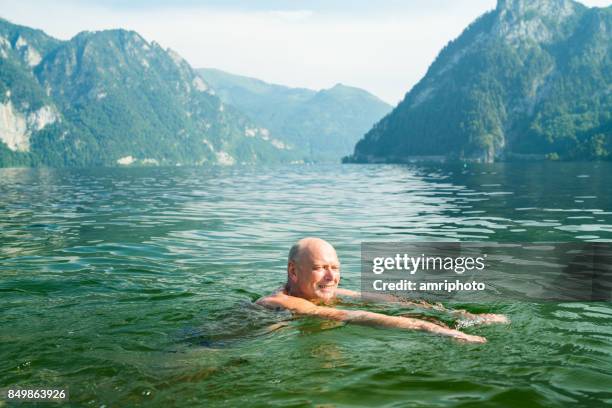 senioren nehmen auf der welt - 70 jahre alte mann schwimmen im bergsee - 75 years stock-fotos und bilder