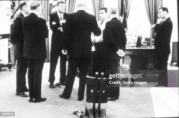 Young John F. Kennedy Jr. Plays under President Kennedy's desk in the Oval Office while his father has a discussion with colleagues October 1963 in...