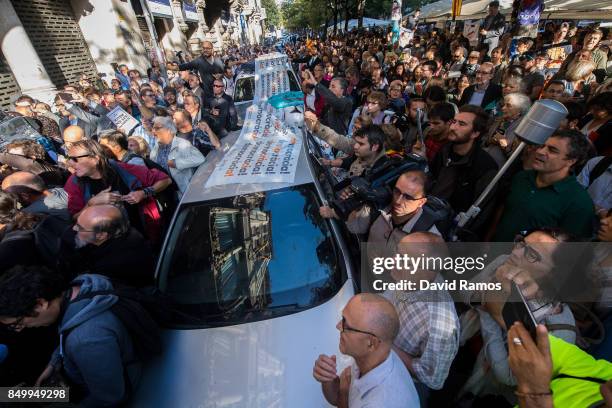 People surround Spanish Civil Guard Police cars outside the Catalan Vice-President and Economy office as police officers hold a searching operation...