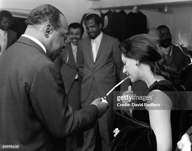 American jazz pianist and composer Count Basie lights a cigarette in its holder for Princess Margaret, Countess of Snowdon backstage during the...