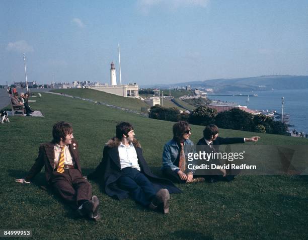 From left, John Lennon, Paul McCartney, George Harrison and Ringo Starr of English rock group The Beatles sit together on Plymouth Hoe during filming...