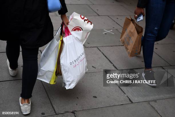 Pedestrians carry Primark and Debenhams branded shopping bags as they walk past shops in central London on September 20, 2017. - British retail sales...