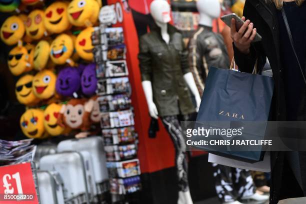 Pedestrians carry shopping bags as they walk past shops in central London on September 20, 2017. British retail sales defied rising prices caused by...