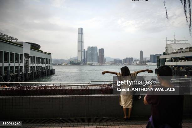 Woman poses while facing Victoria Harbour and the Kowloon skyline as her friend takes photos of her in Hong Kong on September 20, 2017.