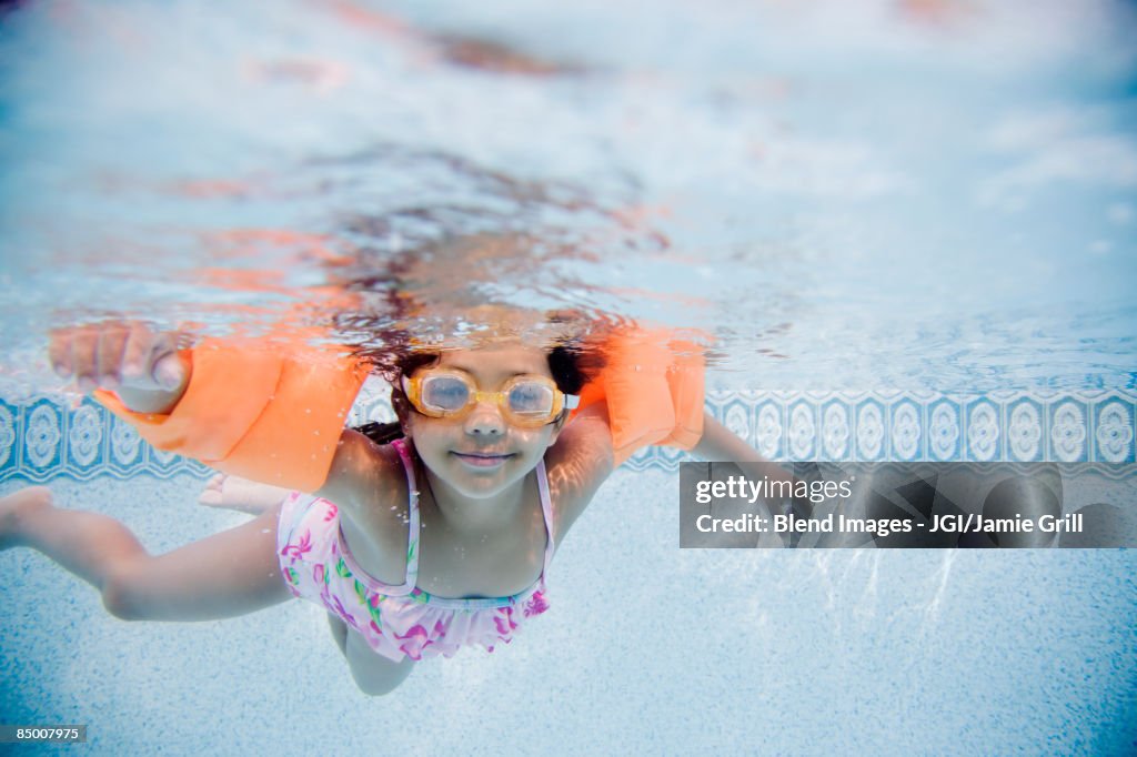 Hispanic girl swimming underwater in pool