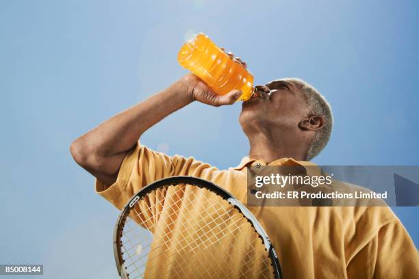 african man drinking juice with tennis racquet - energydrink stock-fotos und bilder