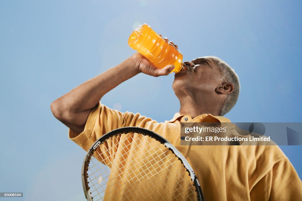 African man drinking juice with tennis racquet