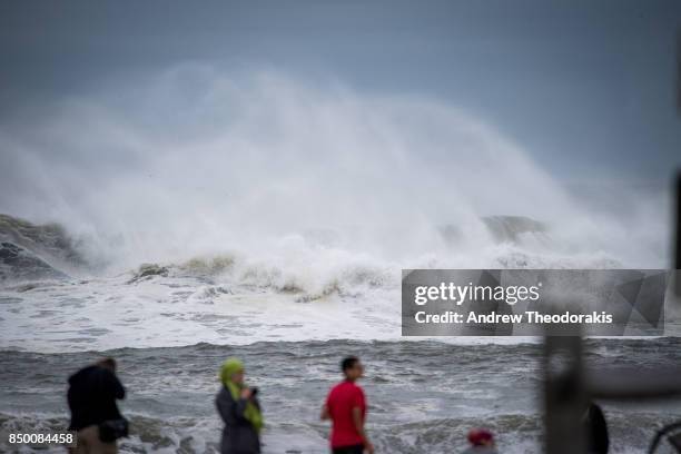 People walk along the beach as high waves produced by Hurricane Jose crash along the shore on September 20, 2017 at Long Island's Smith's Point Beach...