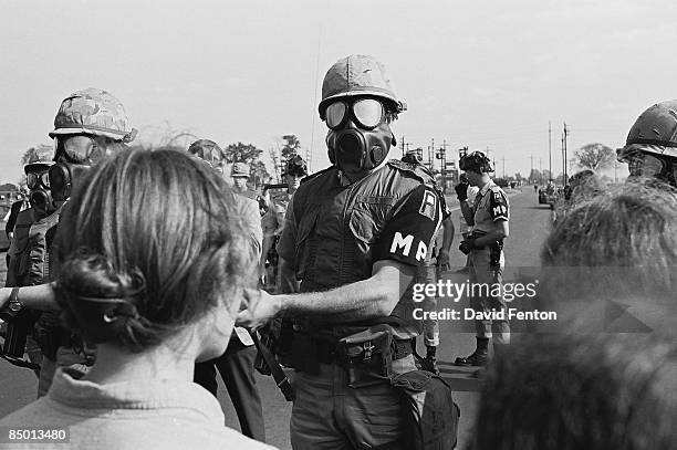 Line of armed MPs from the United States First Army, who wear gas masks and hold rifles with fixed bayonets, confront demonstrators at Fort Dix, New...