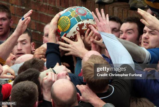 Hands of rival teams Up'ards and Down'ards battle for the ball, which bursts out of the 'hug' under sheer pressure, in the annual Shrove Tuesday 'no...