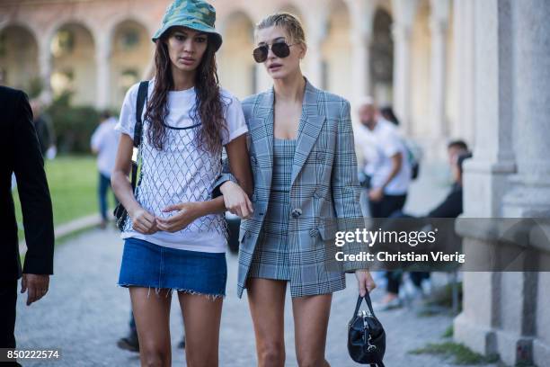 Model Joan Smalls wearing a camouflage hat, white tshirt, denim skirt and model Hailey Baldwin wearing a grey checked dress, grey checked blazer...