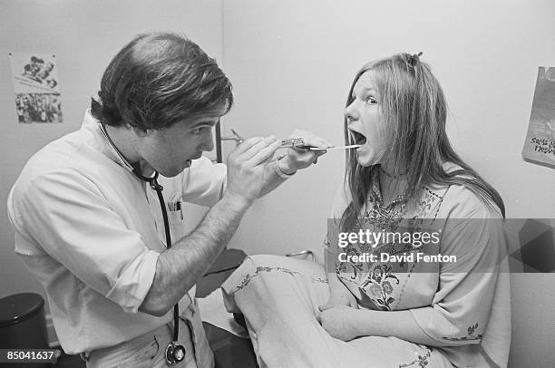 An unidentified young woman sits cross-legged on a examination table as a doctor looks inside her mouth with a pen light at the Free People's Clinic,...