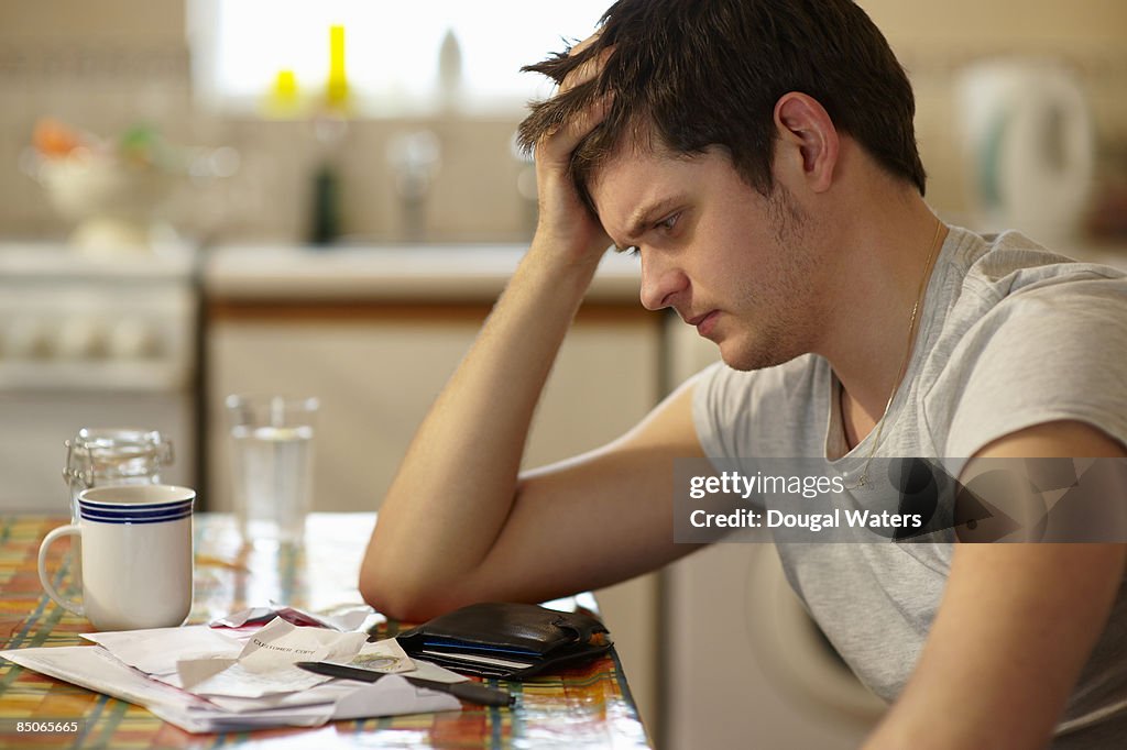Young man holding head looking at receipts.