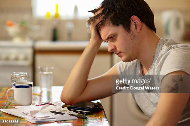young man holding head looking at receipts. - upset man stock pictures, royalty-free photos & images