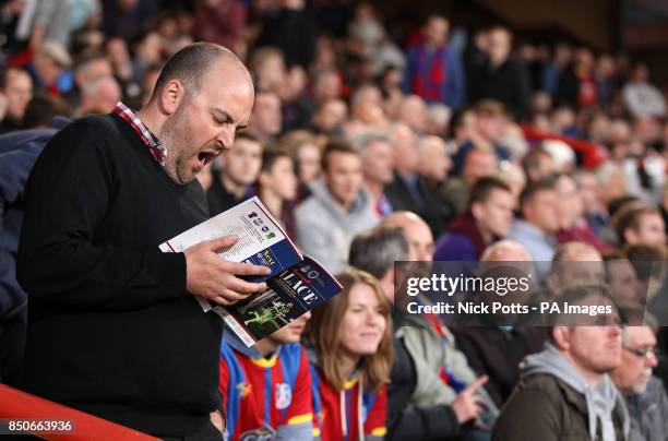 Crystal Palace fan reads the matchday programme in the stands