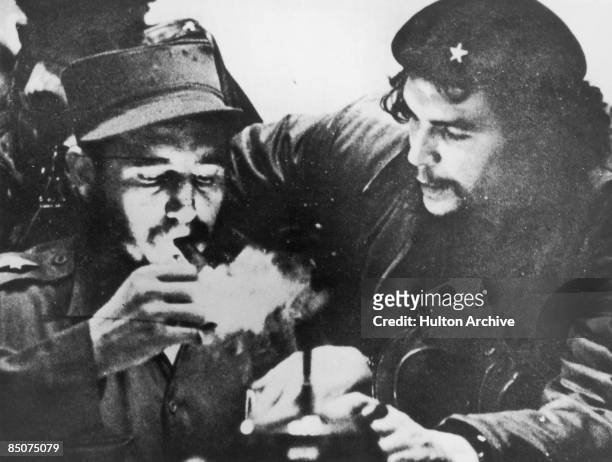 Cuban revolutionary Fidel Castro lights his cigar while Argentine revolutionary Che Guevara looks on in the early days of their guerrilla campaign in...