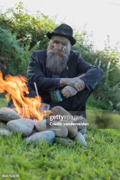 eine alte tramp wärmt sich am lagerfeuer - landstreicher stock-fotos und bilder