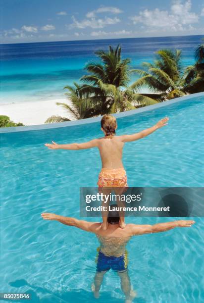 young boy standing up on father shoulders in pool - fregate stock pictures, royalty-free photos & images