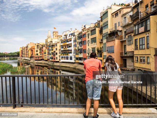 a pair of young women looking from on a bridge, cathedral and houses on onyar riverbank, spain, catalonia, girona. - rivière onyar photos et images de collection